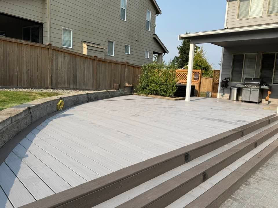 Curved grey composite deck meeting a stone block retaining wall, with contrasting brown step fascia