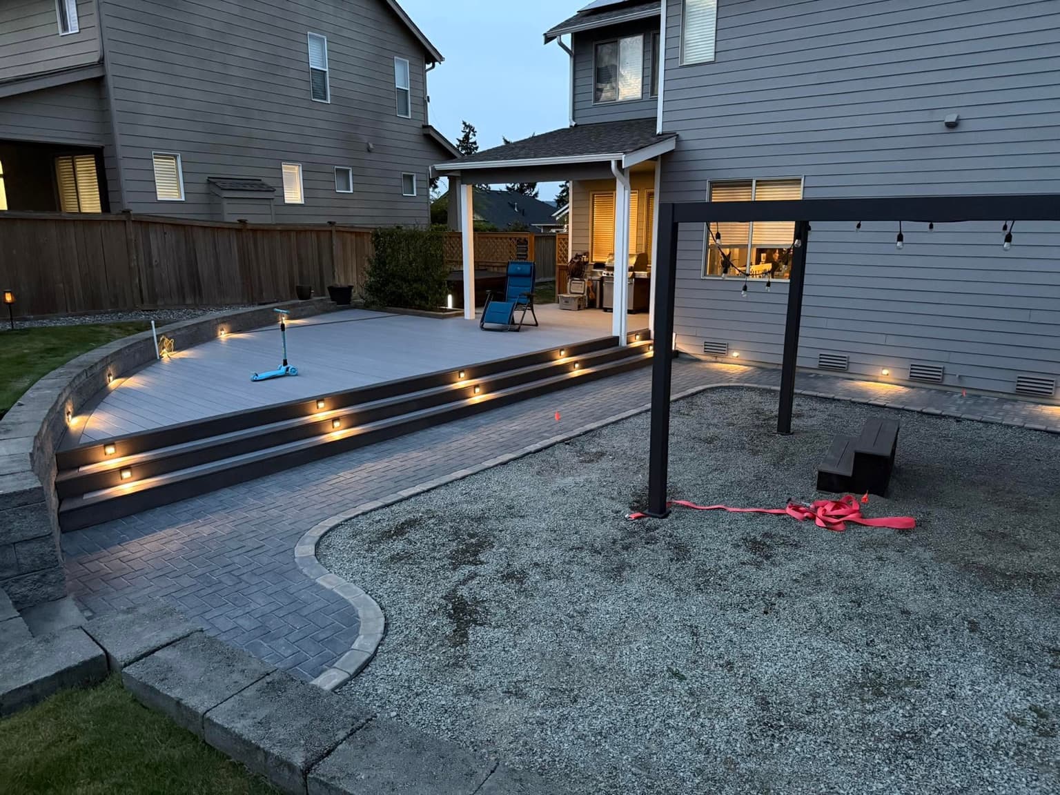 Composite deck with lit steps, herringbone paver patio and a steel pergola at dusk, built by Best Pro Contractors