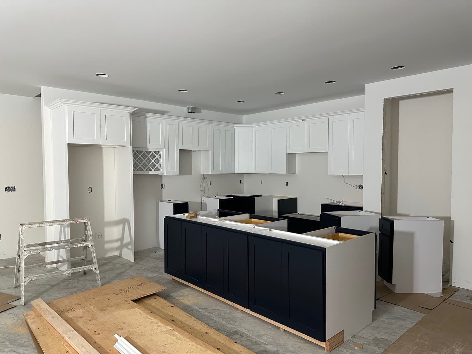 Kitchen with white shaker upper cabinets and a navy island and base run, part way through installation