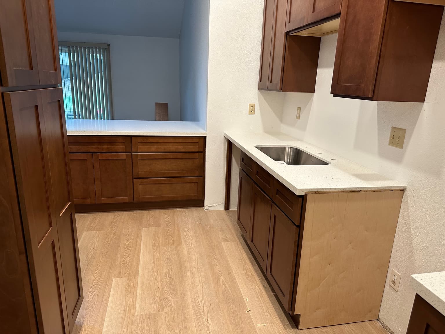 Finished kitchenette with dark shaker cabinets, quartz countertop, undermount stainless sink and light plank flooring